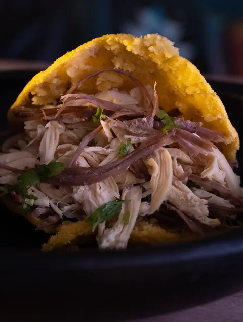 Arepa de maíz rellena de carne desmechada, fondo oscuro.
